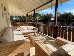 An outdoor seating area with wooden furniture and a view of a pool and palm trees.