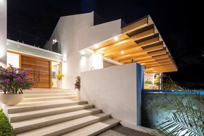 Une maison moderne avec un escalier menant à une porte en bois, une piscine et des plantes en pot.