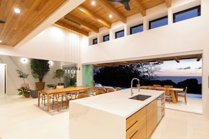 Una cocina moderna con una isla grande, vigas de madera en el techo y vista al mar.
