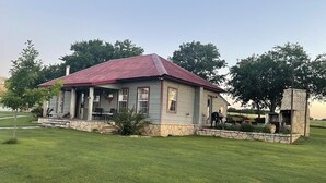 A house with a red roof, stone foundation, and a patio area with outdoor seating. - Country Cottage on Weatherford Ranch (Weatherford)