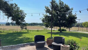 An outdoor seating area with wicker chairs and a large planter, surrounded by a gravel path and greenery. - Country Cottage on Weatherford Ranch (Weatherford)