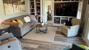 A living room with a grey sofa, patterned armchairs, a coffee table, and a bookshelf. - Country Cottage on Weatherford Ranch (Weatherford)