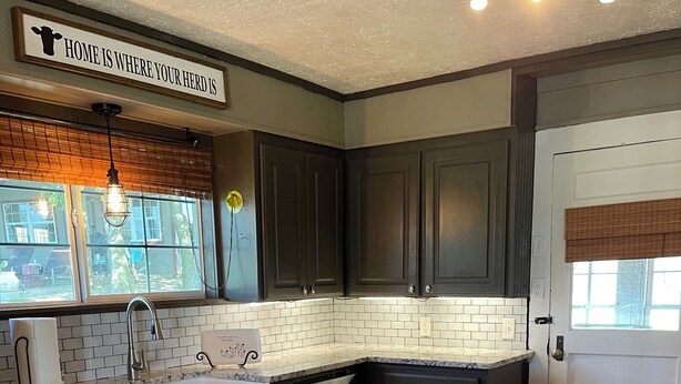 A modern kitchen with dark cabinets, a white tiled backsplash, and a central island with yellow stools. - Country Cottage on Weatherford Ranch (Weatherford)