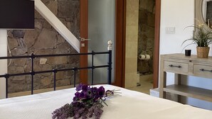 Un dormitorio con cama, cabecero de madera, pared de piedra, escalera, baño con espejo y planta en maceta.