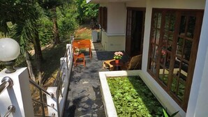 Ein schmaler Pfad führt zu einem Haus mit einem kleinen Garten, einer hölzernen Bank und einem Tisch mit Blumen.