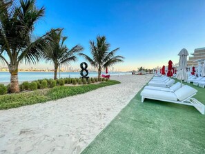 Ett hotell vid stranden med vita solstolar, palmer och en fri utsikt över stadens silhuett.