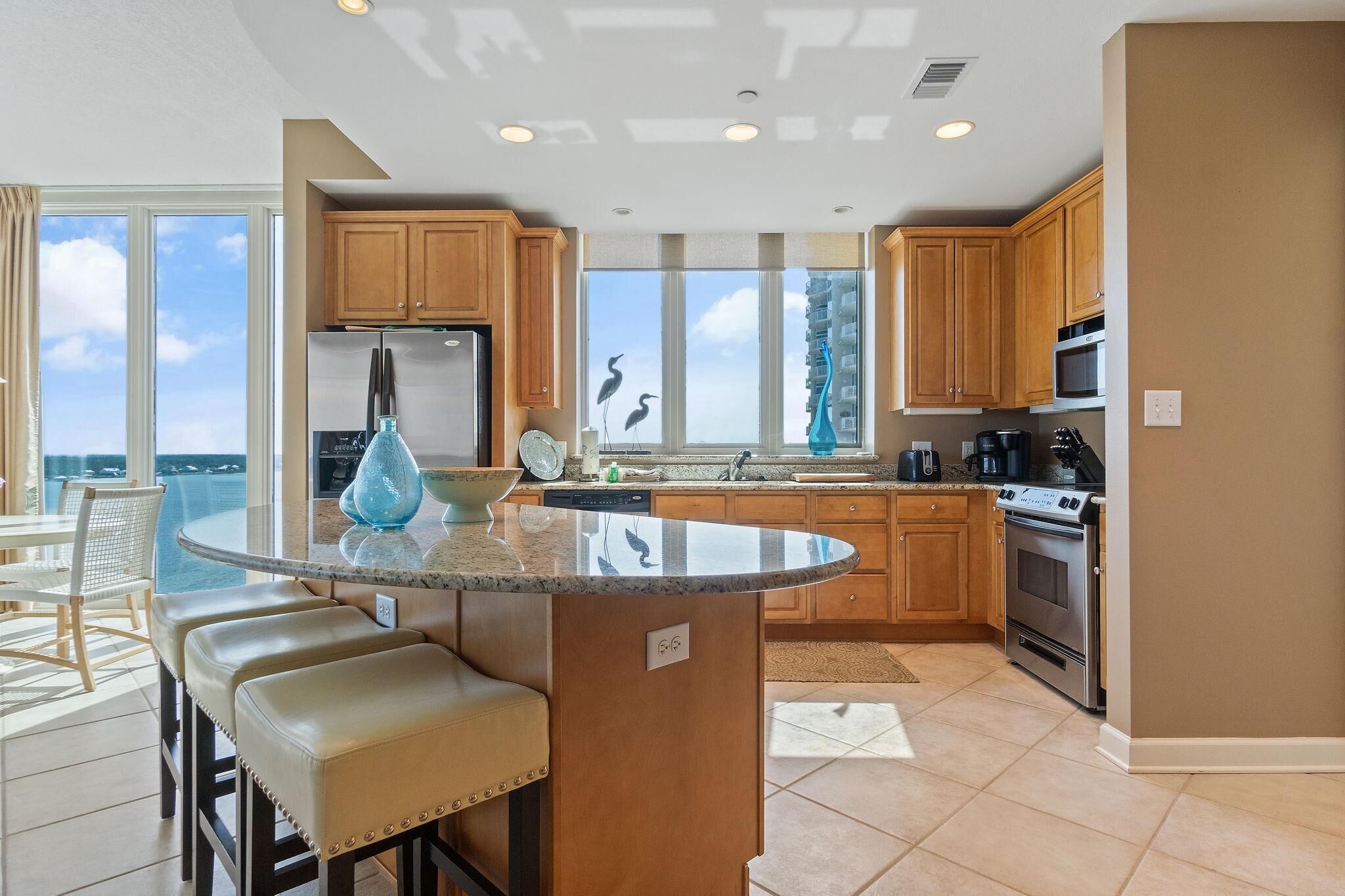 A modern kitchen with wooden cabinets, a stainless steel refrigerator, a dishwasher, and a large island with bar stools.
