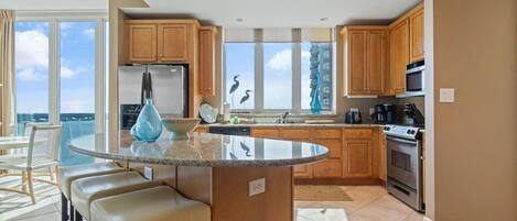 A modern kitchen with wooden cabinets, a stainless steel refrigerator, a dishwasher, and a large island with bar stools.