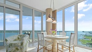 A balcony with a view of the sea, a round table with chairs, and a hanging light fixture. - Lagoon Tower 1002 (Gulf Shores)