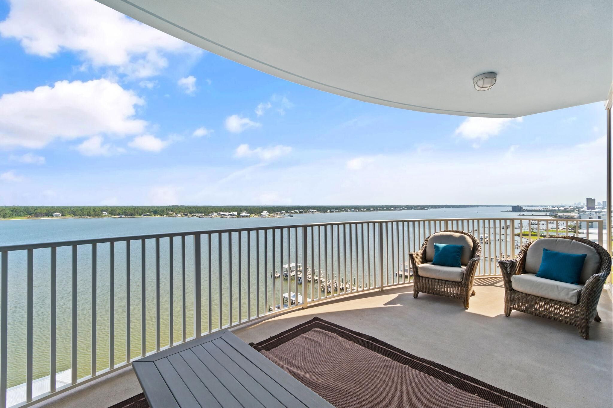 A balcony with wicker chairs and a view of a lake and city skyline.