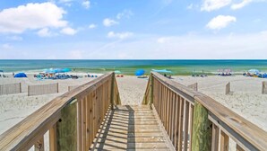 A wooden boardwalk leading to a sandy beach with umbrellas and beach chairs. - Lagoon Tower 1002 (Gulf Shores)
