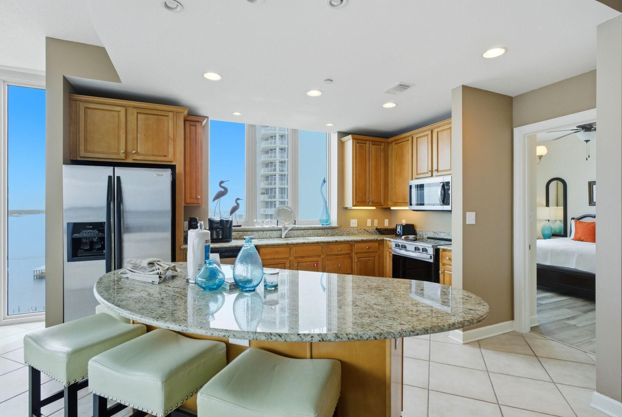 A modern kitchen with granite countertops, wooden cabinets, a built-in oven, and a large island with bar stools.