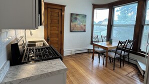 A kitchen with a gas stove, wooden cabinets, a dining table with chairs, and a view through large windows.