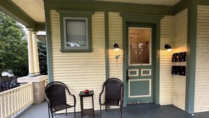 A covered porch with two wicker chairs and a small table, a door with a mailbox, and a wall-mounted light fixture.