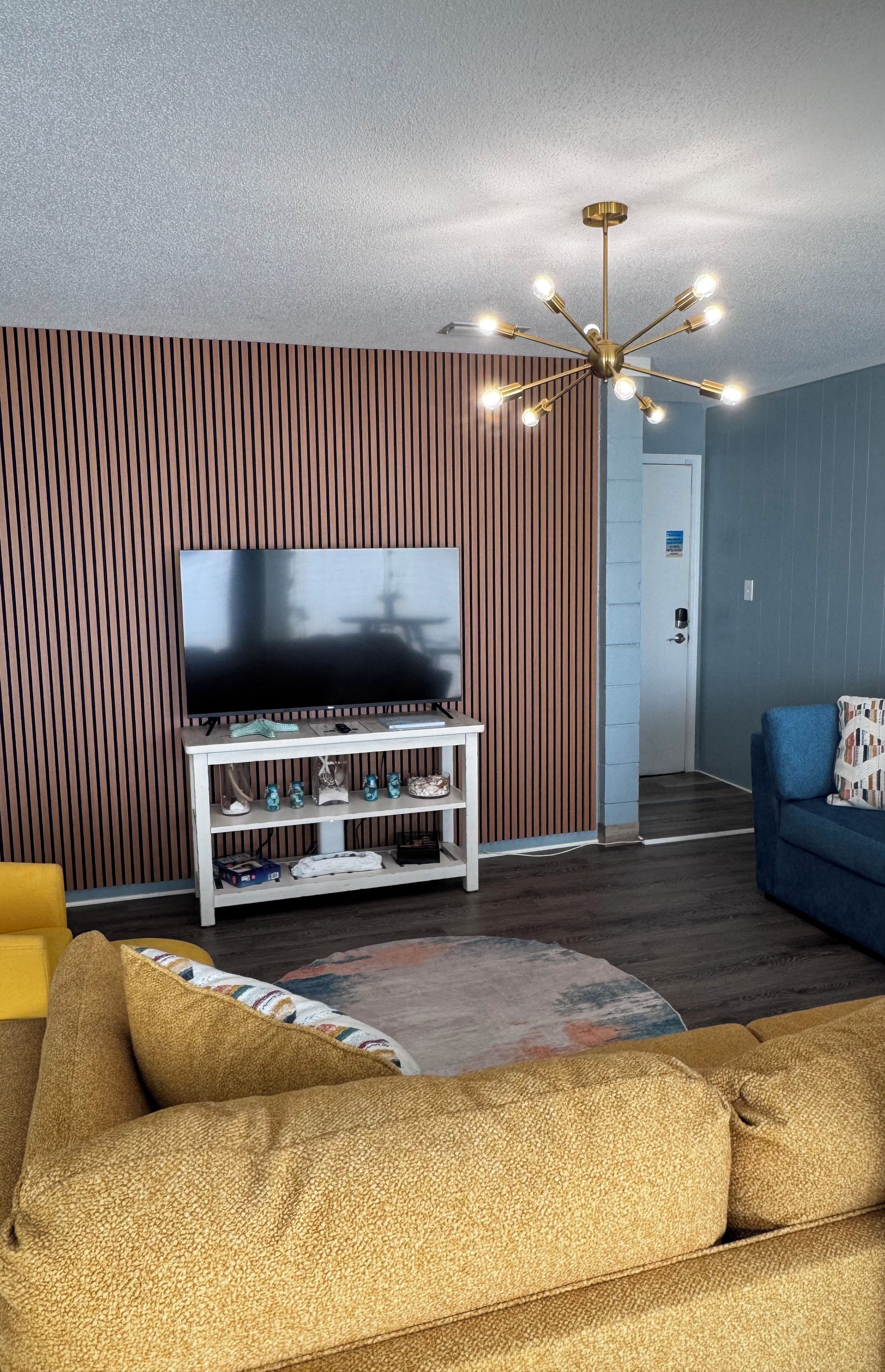 Ein modernes Wohnzimmer mit einem Flachbildfernseher auf einem weißen Schrank, einer braunen Wand mit Muster, einem blauen Sofa und einer Mehrlicht-Kronleuchter.