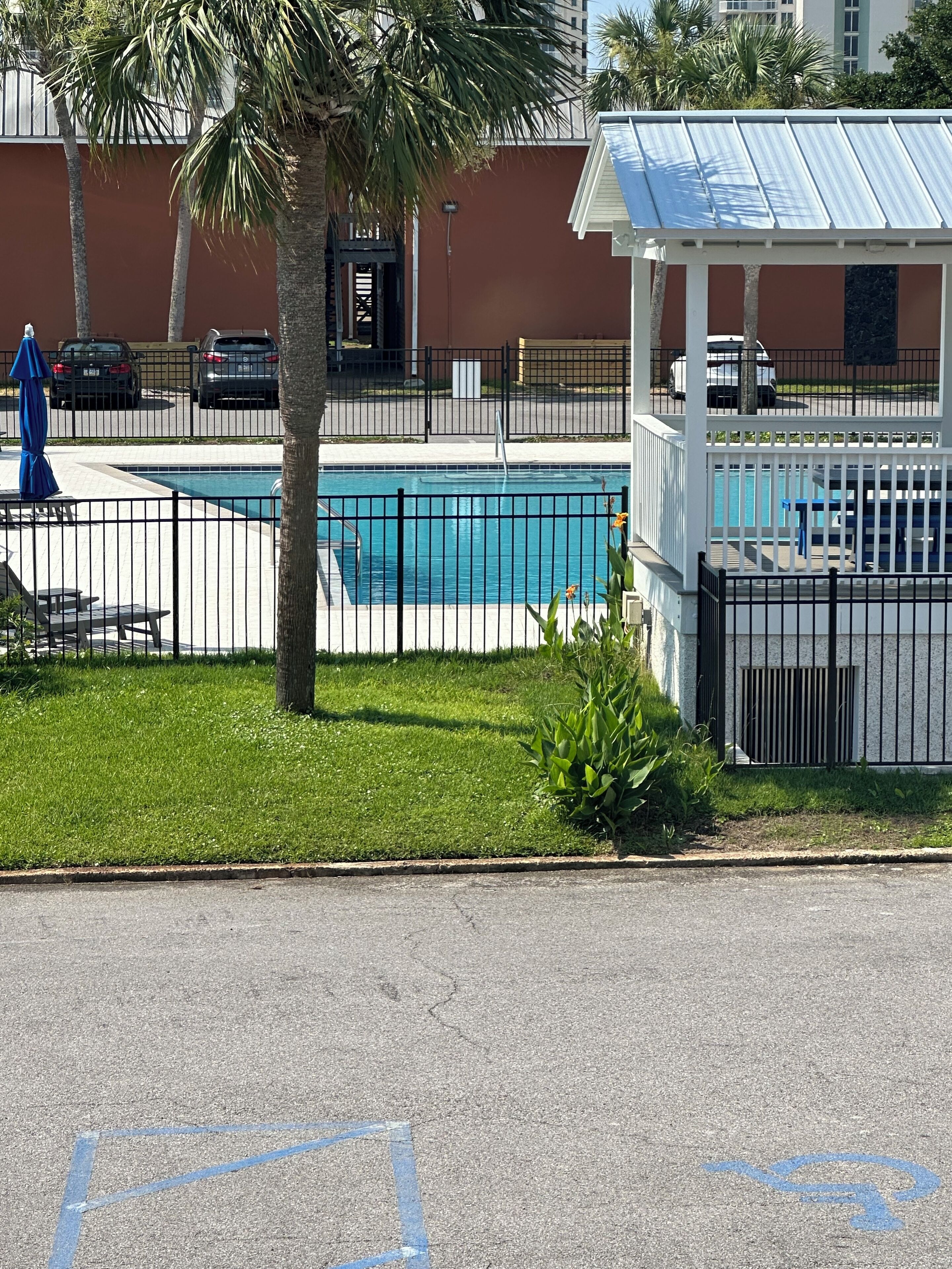 A swimming pool with a fenced area, a covered seating area, and a building in the background.
