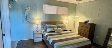 Ein Schlafzimmer mit Bett, Nachttischen, Deckenventilator, Kommode und Wandfernseher.