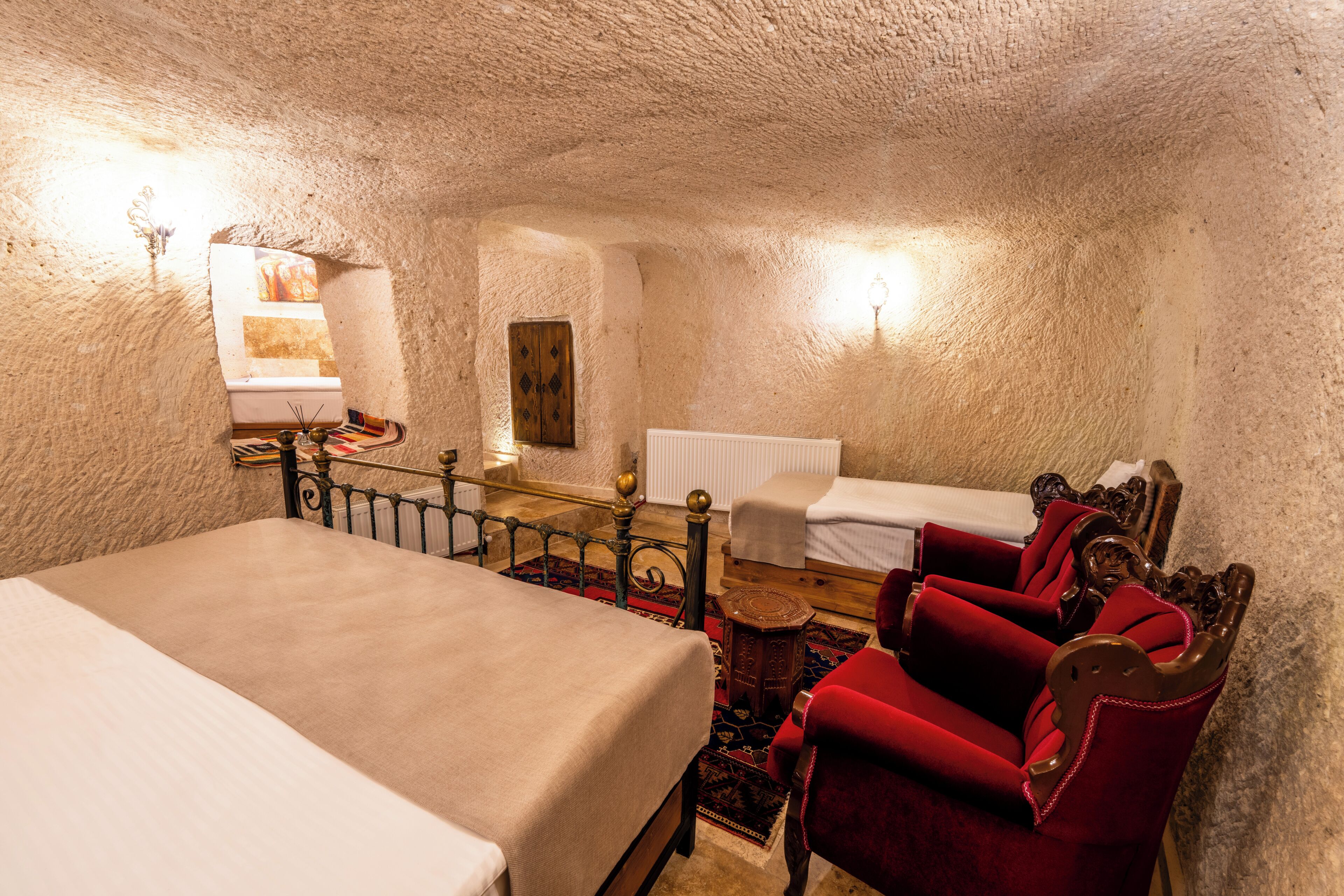Ein Schlafzimmer mit einem großen Bett, einem kleineren Bett, einem roten Sessel, einer Holzbank und einer Heizung.