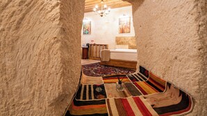 A cozy, rustic interior with a wooden ceiling, a bed with a colorful striped rug, and a chandelier. - Library Cave Hotel (Urgup)