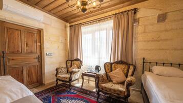 A room with two wooden chairs, a small table, a bed, and a large window with curtains.