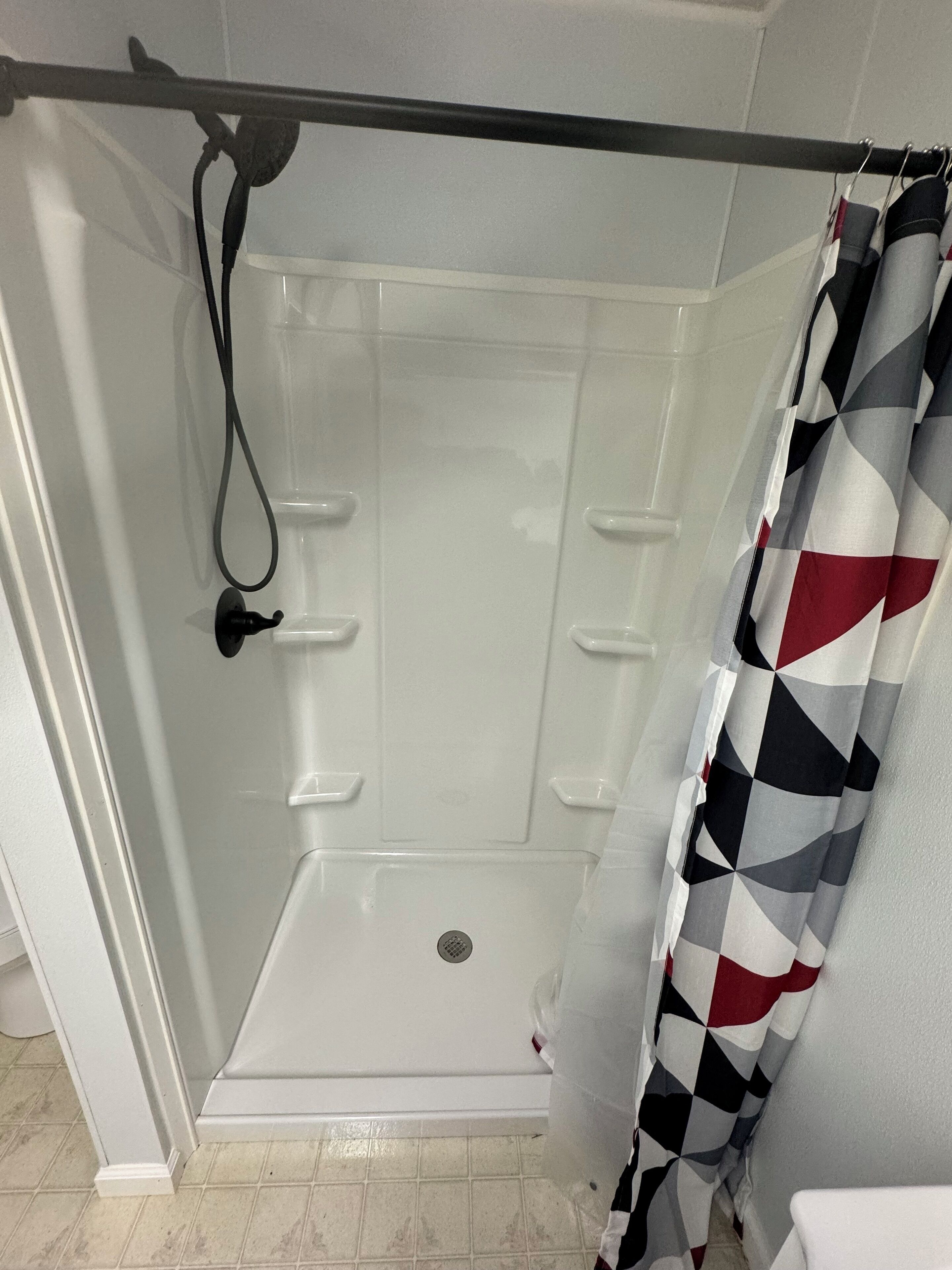 Un espace douche doté d’une porte en verre, d’un panneau de commande de douche et d’un rideau de douche à motifs.
