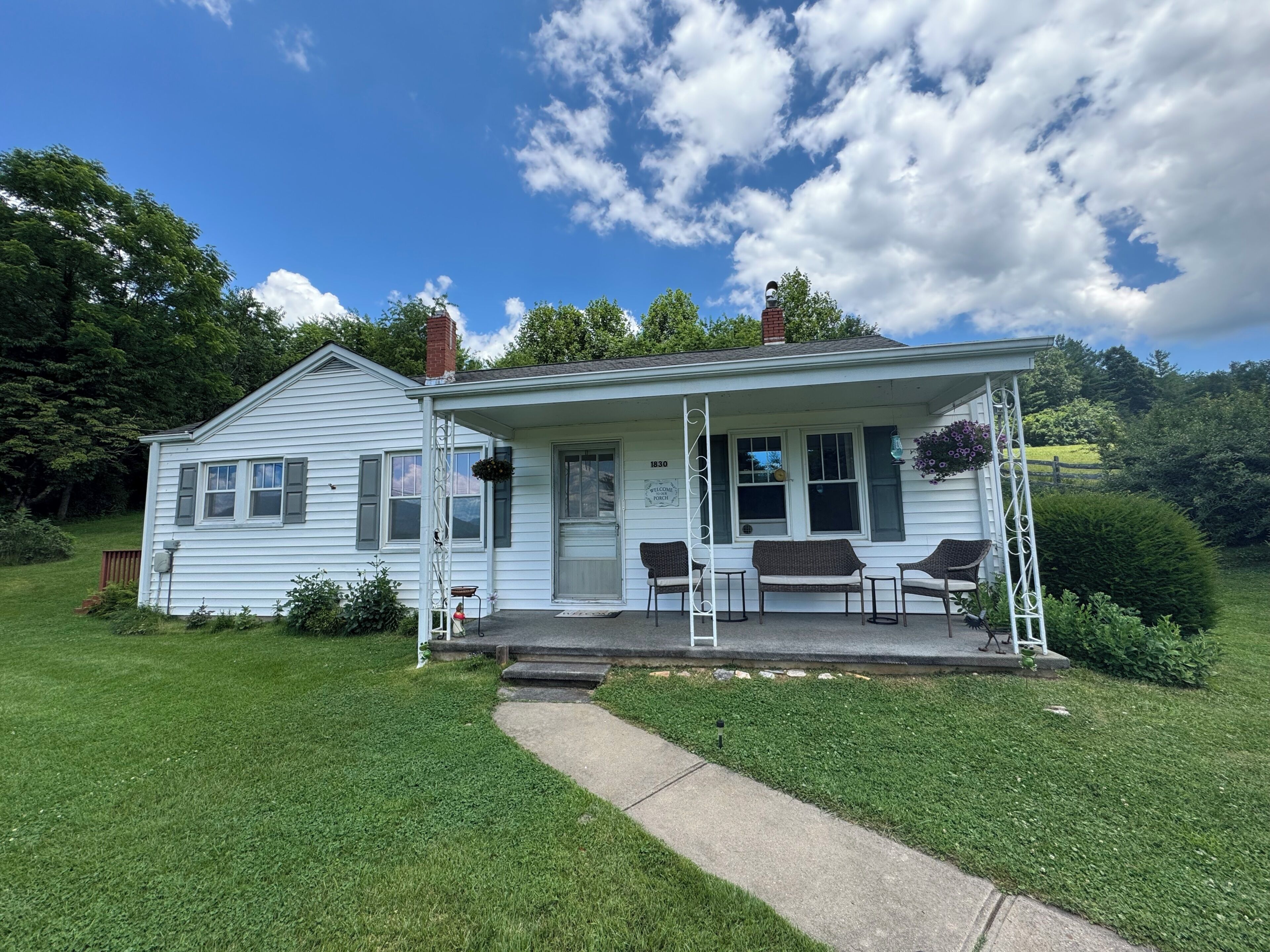 A white two-story house with a porch, a number '1830' sign, and a small garden.