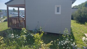 Ein kleines, einstöckiges Gebäude mit geneigtem Dach und einem kleinen Fenster. An einer Seite ist eine Holzterrasse angebaut.