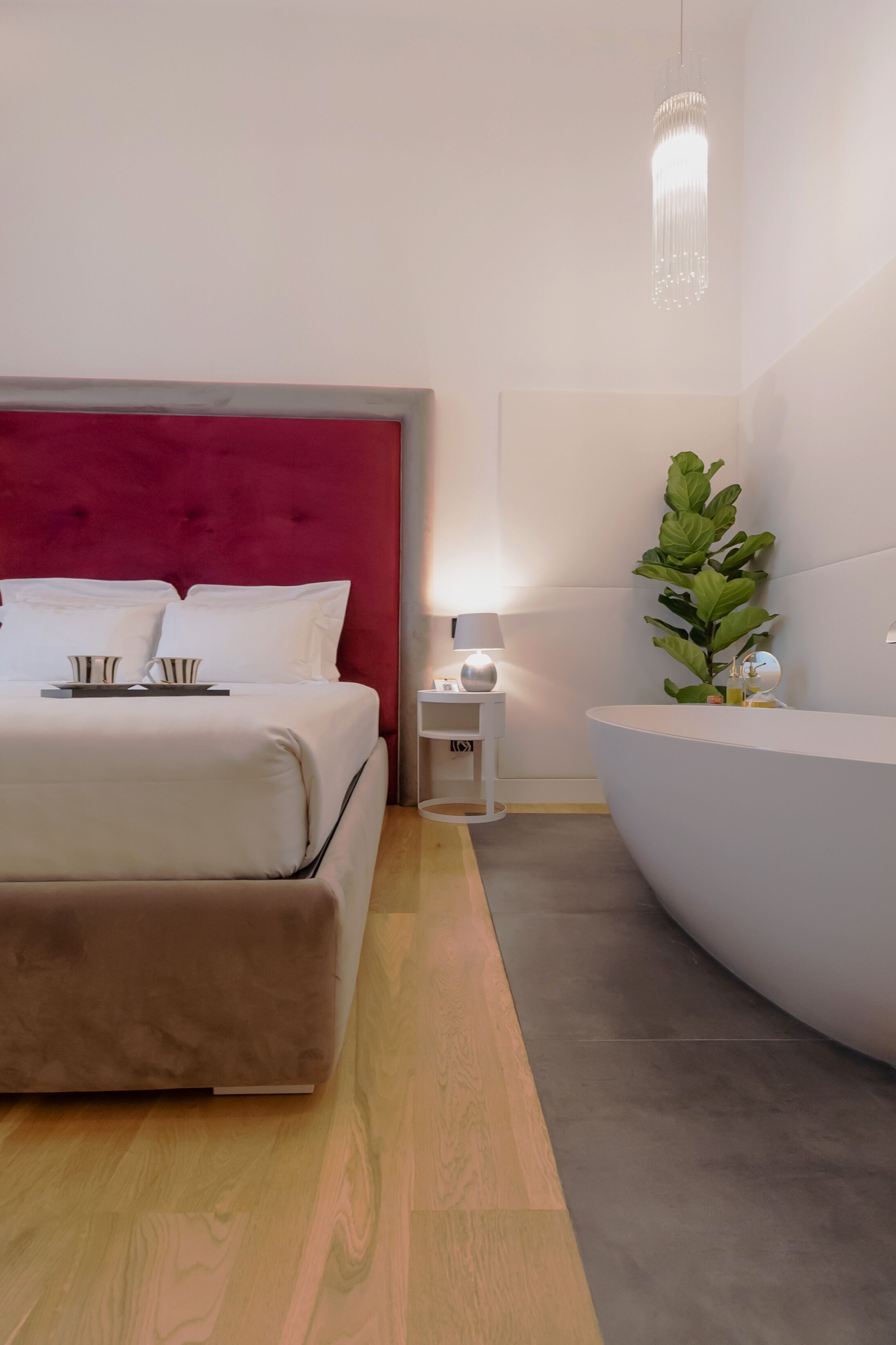 A modern hotel room with a large bed, bedside table, and a plant.
