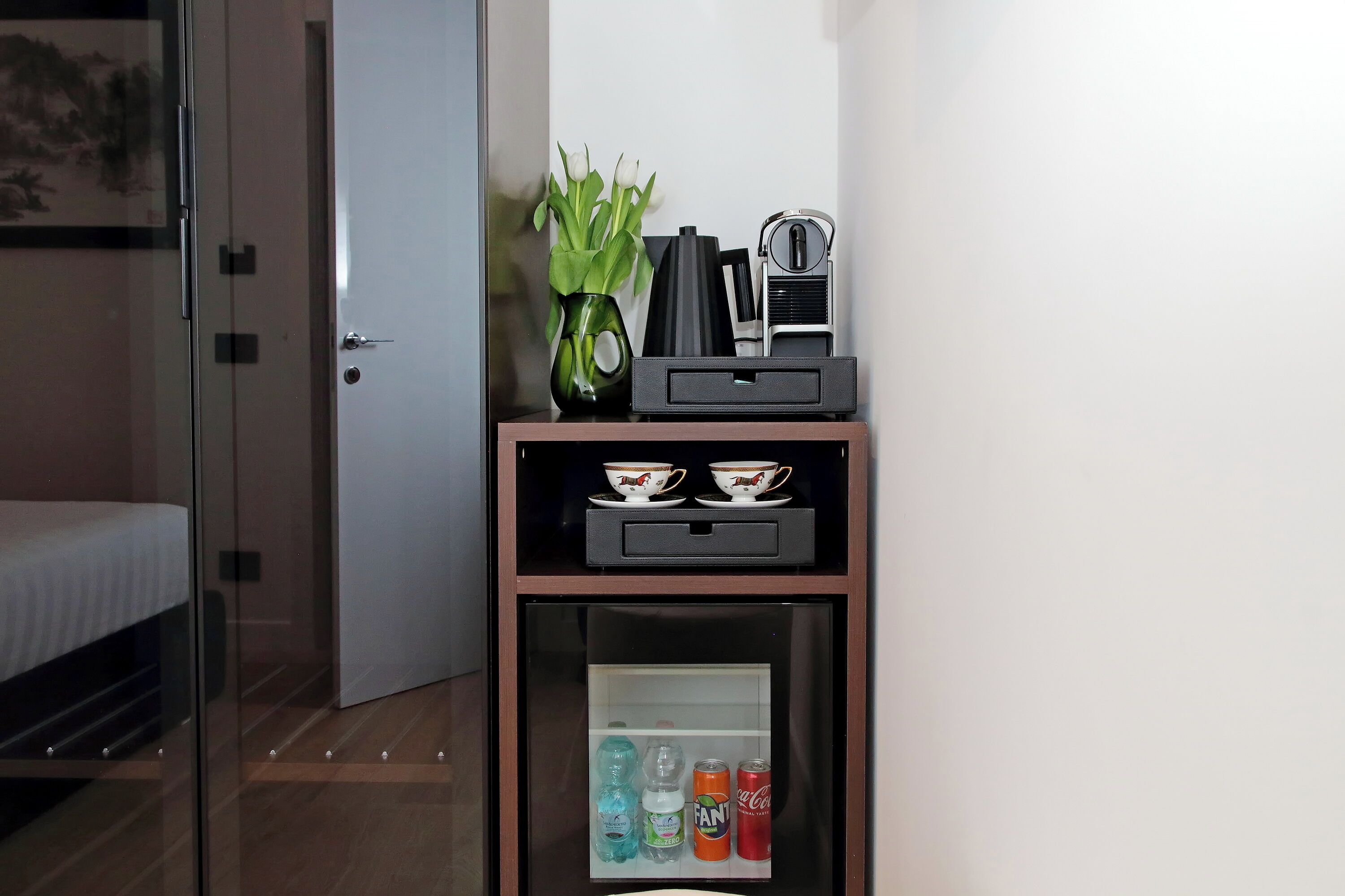 Une chambre d’hôtel équipée d’un mini-bar contenant une machine à café, des tasses et un vase avec des fleurs.