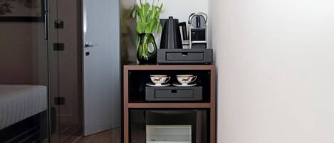 Une chambre d’hôtel équipée d’un mini-bar contenant une machine à café, des tasses et un vase avec des fleurs.