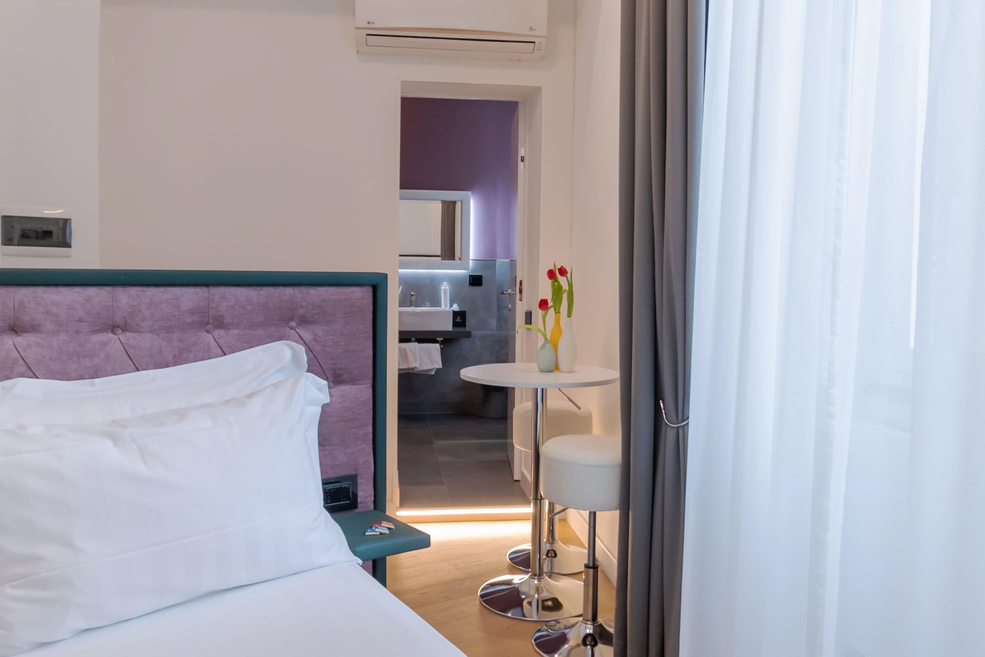 Een hotelkamer met een bed, een klein tafeltje met een vaas, en uitzicht op de badkamer en keuken.