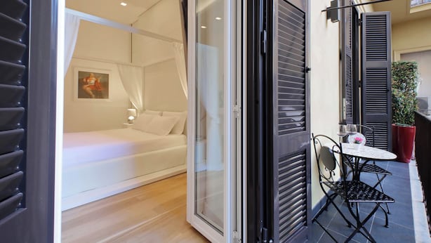 A modern bedroom with a glass door leading to a balcony, a white sofa, and a small table with a vase. - Domus Aurea Luxury Suites (Rome)