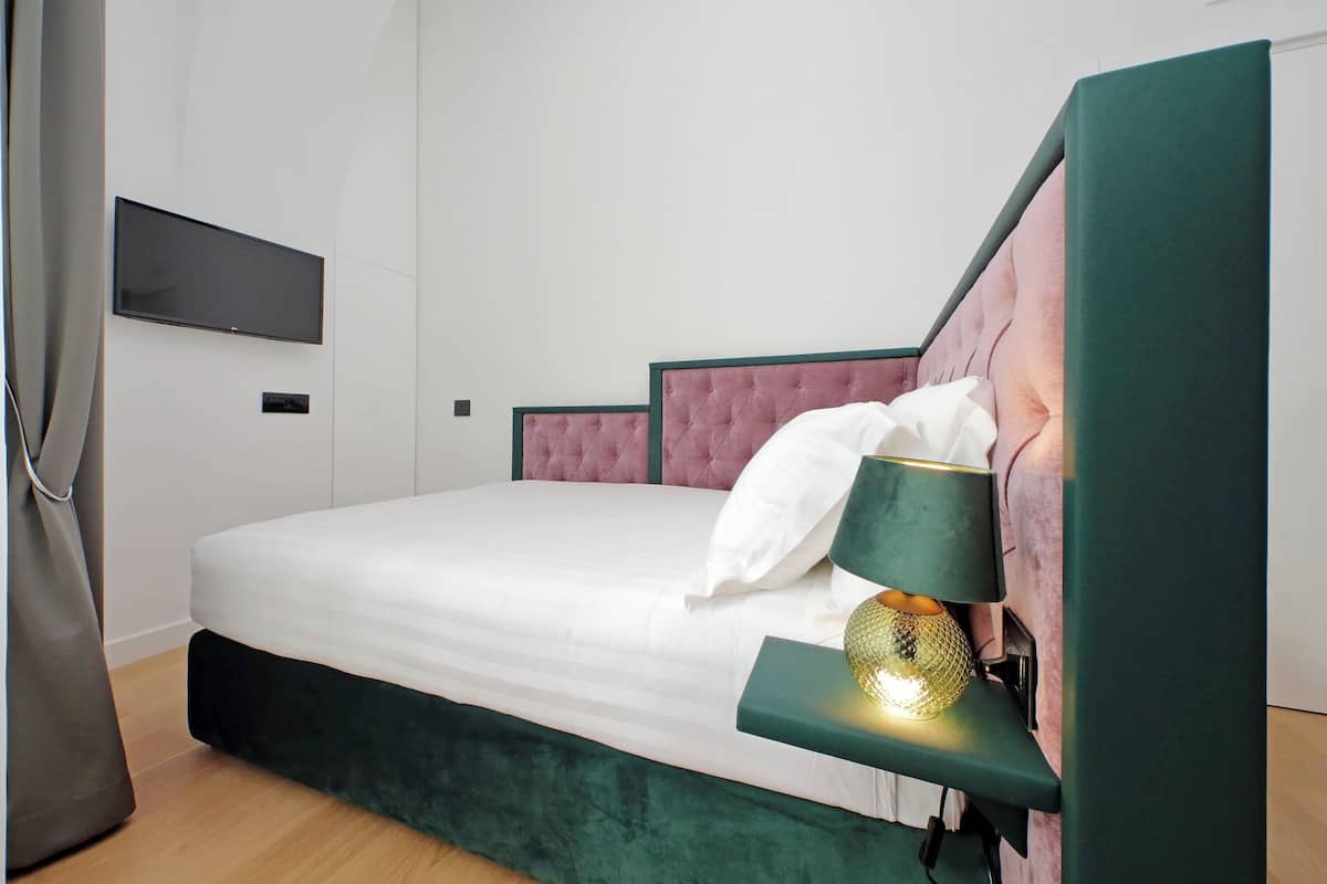 A neatly made bed with a green headboard, a bedside lamp, and a flat-screen TV mounted on the wall.
