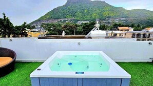 A hot tub on a rooftop with a view of a mountain and residential buildings. - 4 Bedroom Private Villa Villa La Tourelle (Tamarin)