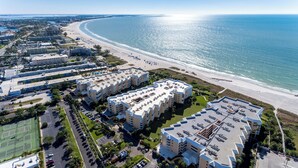 An aerial view of a coastal hotel complex with multiple buildings, a beach, and a tennis court.