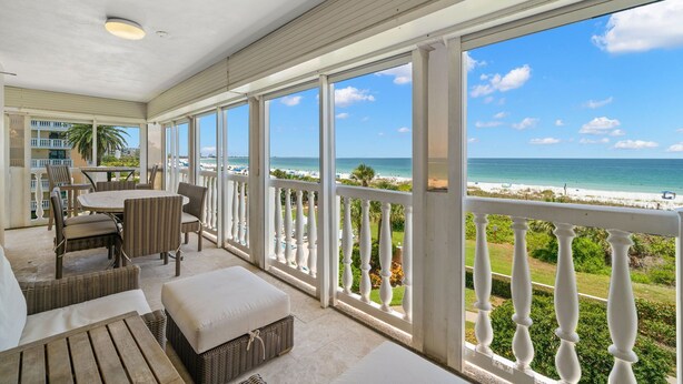 A covered outdoor area with a view of the beach, furnished with wicker chairs and a table.