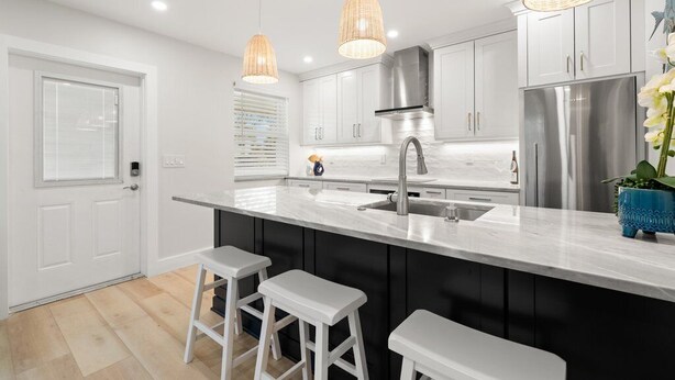 Una cocina moderna con armarios blancos, un refrigerador de acero inoxidable y una isla central con taburetes de bar.