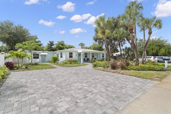 A light blue building with a paved driveway and palm trees.
