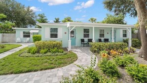 A light blue single-story house with a covered porch, a small garden, and a paved driveway.