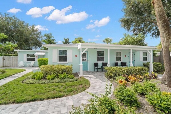 Ett ljusblått, enplanshus med en inglasad veranda, en liten trädgård och en asfalterad uppfart.