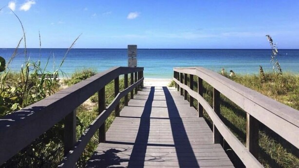 A wooden boardwalk leading to a beach with clear blue water and a clear sky.