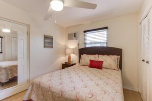 A bedroom with a bed, a nightstand, a ceiling fan, a window with blinds, and a door.