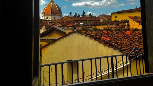 A view of a domed building with a tiled roof and a yellow building in the foreground. - Elegante Appartamento Vista sul Duomo di Firenze  (Firenze)