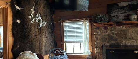 A cozy cabin interior with a large fur rug, a television mounted on the wall, a fireplace, and a sign that reads "Buffalo Horizon".