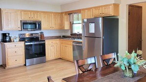 Une cuisine moderne avec des meubles en bois, des appareils électroménagers en acier inoxydable et un coin repas comprenant une table et des chaises en bois.