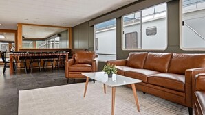 Un intérieur moderne avec un canapé en cuir marron, une table basse en verre et un coin repas comprenant des chaises et une table.