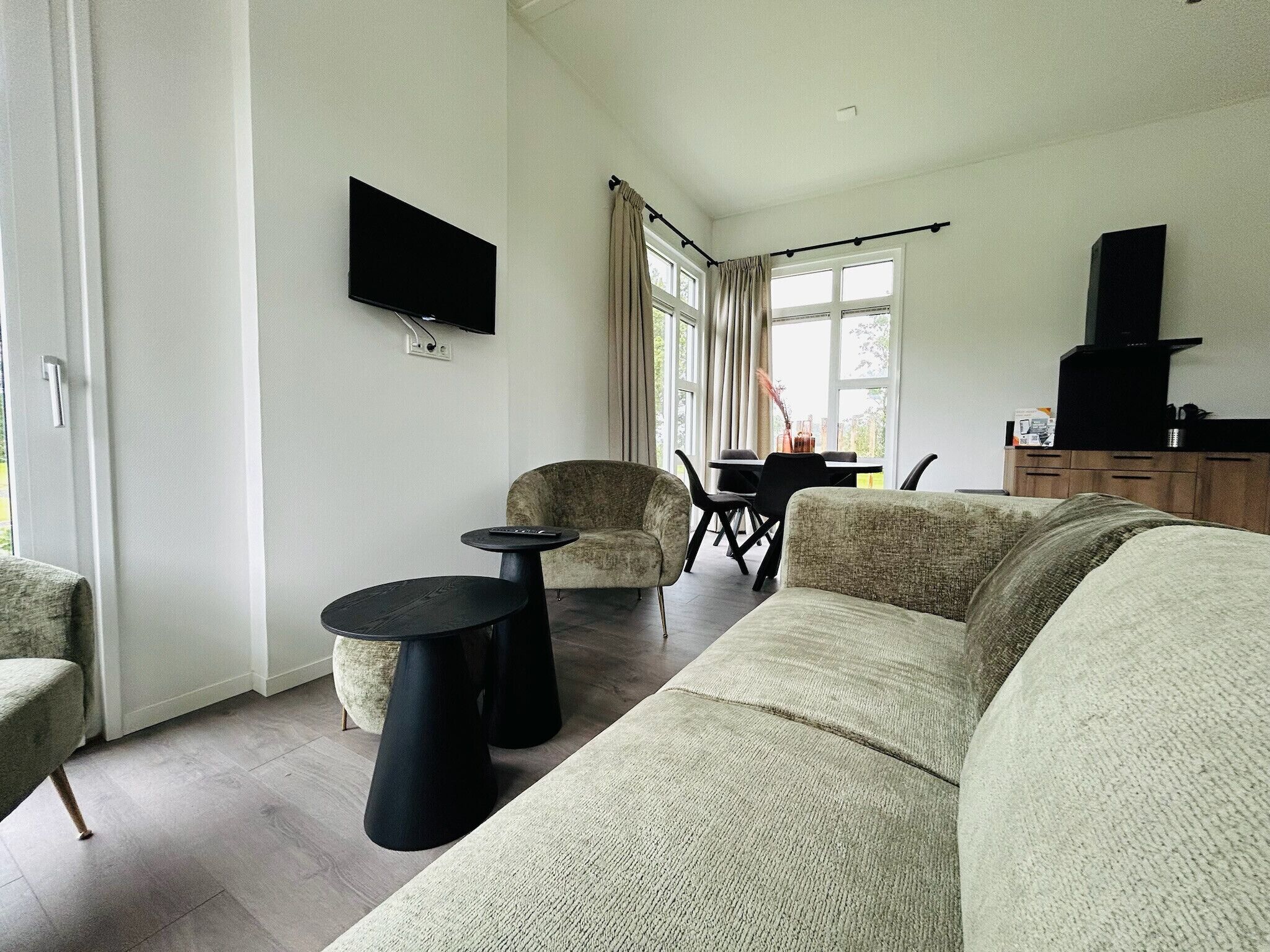 Un salon comprenant un canapé, deux fauteuils, une table basse, un téléviseur à écran plat fixé au mur, et un coin repas avec une table et des chaises.