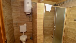 Ein kleines Badezimmer mit Toilette, Duschkabine und Warmwasserbereiter.