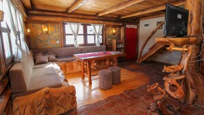 Ein rustikales Blockhaus-Interieur mit Steinwand, Holzbalkendecke, einer Couch, einem Tisch und einer außergewöhnlichen Holzbrenntoilette.