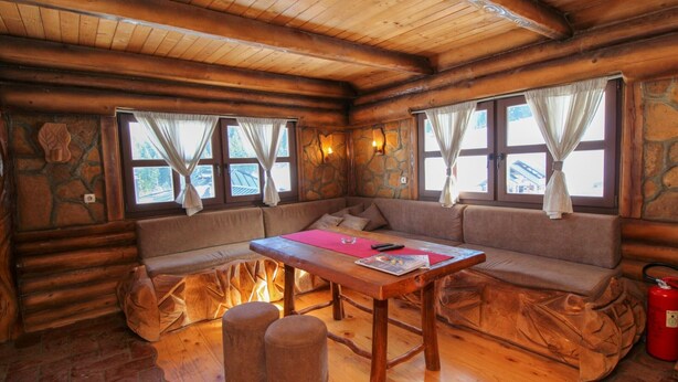 Ein gemütliches Blockhaus-Interieur mit einem Holztisch, gepolsterten Sitzgelegenheiten und Steinwänden.